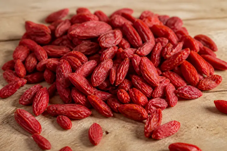 Petites baies de goji séchées de couleur rouge vif disposées sur une table en bois clair.