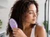 Comment choisir sa brosse démêlante pour cheveux bouclés ? Une femme tient délicatement une brosse démêlante cheveux bouclés dans sa salle de bain lumineuse
