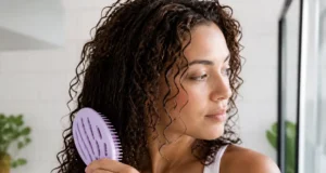 Comment choisir sa brosse démêlante pour cheveux bouclés ? Une femme tient délicatement une brosse démêlante cheveux bouclés dans sa salle de bain lumineuse