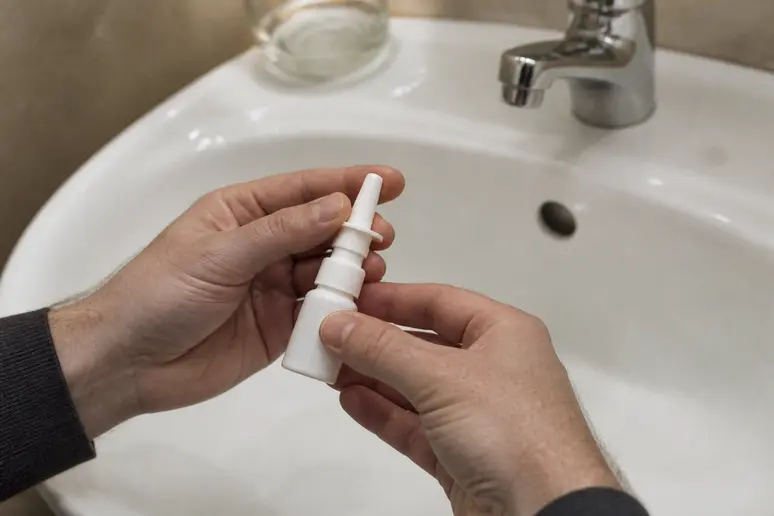 Personne effectuant un lavage nasal avec du sérum physiologique au-dessus du lavabo