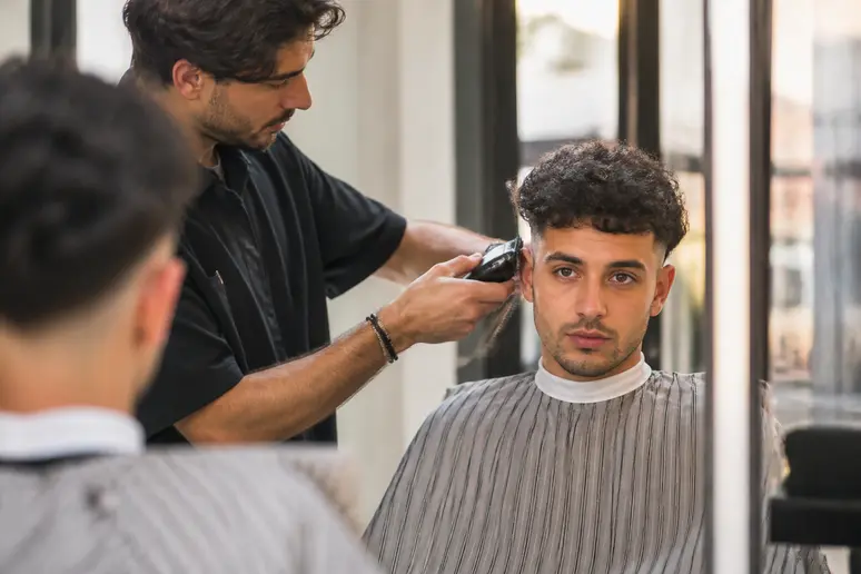 Homme parisien aux coupes homme bouclé tendance, obtenant un dégradé chez le coiffeur.