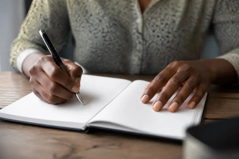 Mains écrivant leurs pensées sur un carnet en papier lors d'une séance de journaling