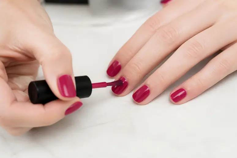 Application minutieuse d'un vernis par une manucuriste, révélant le budget et le savoir-faire d'une manucure.