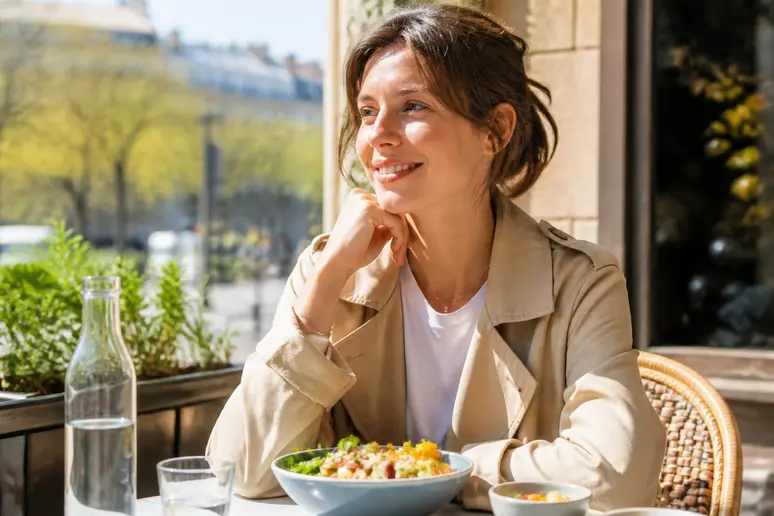 Résultat méthode renata franca avant après sur une femme détendue prenant un repas sain en terrasse parisienne.