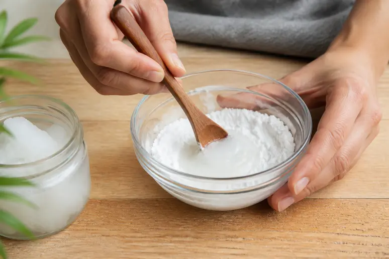 Mains mélangeant du bicarbonate de soude et de l'huile de coco dans un bol pour réduire la transpiration acide.