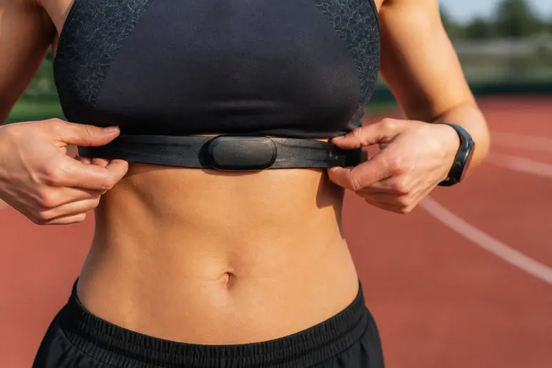 Sportif ajustant une ceinture pectorale de cardiofréquencemètre sur une piste d'athlétisme pour calculer vo2max