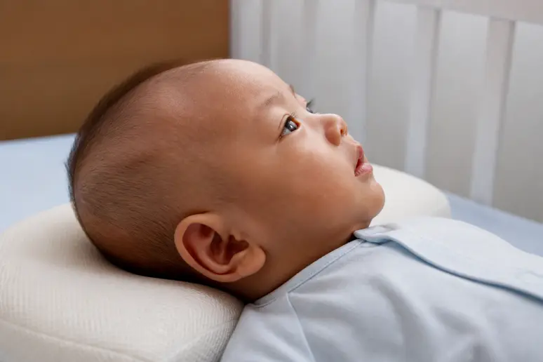 Tête de nouveau né reposant sur un coussin ergonomique de puériculture