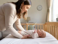 Cocon ergonomique pour bébé et règle du couchage à plat Un parent installe un nourrisson sur le dos dans son lit près d'un cocon ergonomique bébé.