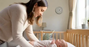 Cocon ergonomique pour bébé et règle du couchage à plat Un parent installe un nourrisson sur le dos dans son lit près d'un cocon ergonomique bébé.