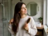 Cure de sébum : avis et conseils face aux démangeaisons Jeune femme brossant doucement ses cheveux longs dans une salle de bain lumineuse pour une cure de sébum avis conseils naturelle