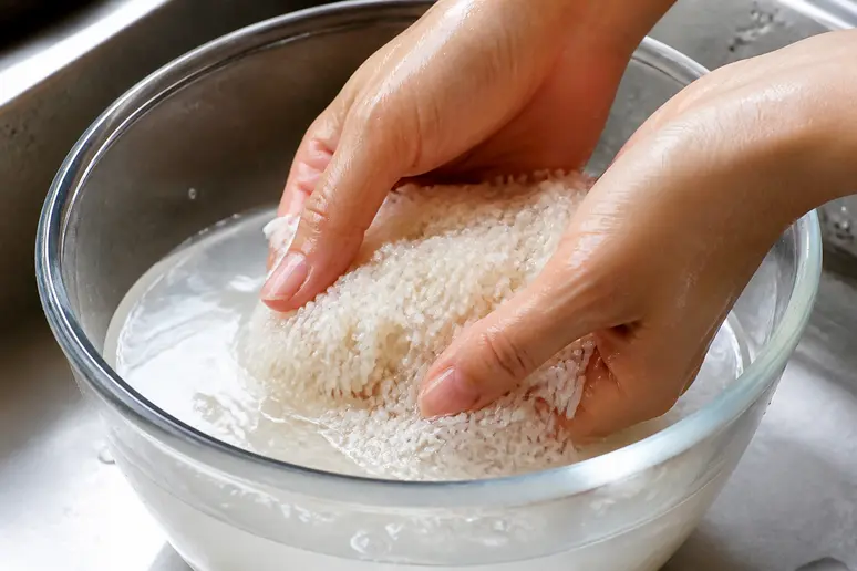 Mains rinçant du riz blanc dans un bol d'eau pour préparer un soin capillaire naturel.