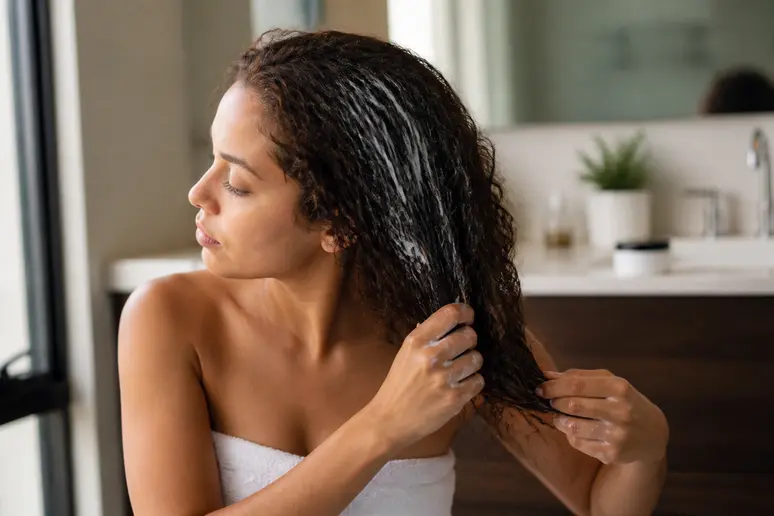 Application d'un masque capillaire nourrissant sur des cheveux bouclés pour éviter l'effet paille.