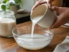 Eau de riz pour les cheveux : pousse, brillance et recette Un flacon contenant de l'eau de riz cheveux posé sur une table en bois dans une cuisine lumineuse.