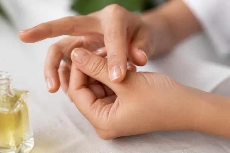 Mains massant délicatement l'huile nourrissante sur le contour des cuticules pour faire pousser ses ongles rapidement
