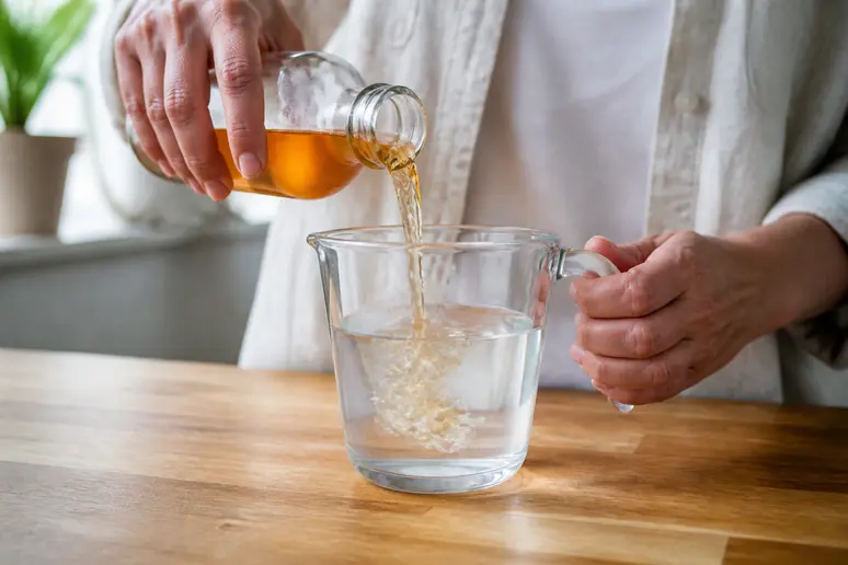 Mains versant du vinaigre de cidre dans un récipient d'eau fraîche pour une eau de rinçage