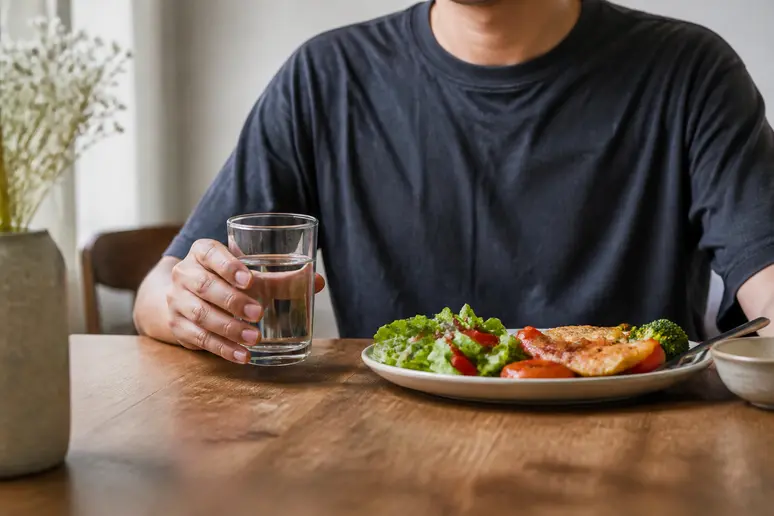 Verre d'eau posé sur une table à côté d'un repas pour illustrer la bonne hydratation.