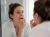 Jaunissement des dents : taches d’émail ou dentine visible ? Femme examinant son sourire devant son miroir de salle de bain pour comprendre le jaunissement des dents