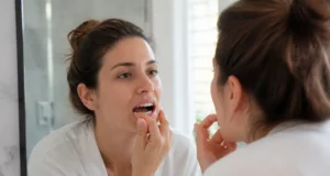 Jaunissement des dents : taches d’émail ou dentine visible ? Femme examinant son sourire devant son miroir de salle de bain pour comprendre le jaunissement des dents