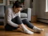 Sens du pied gauche qui gratte entre présage et mycose Une personne assise chez elle examine sa cheville avec un pied gauche qui gratte signification.