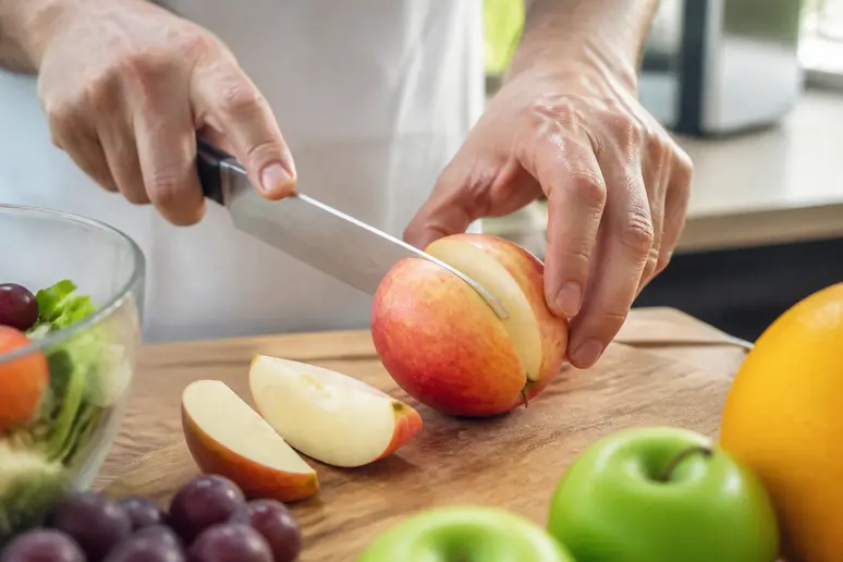 Une personne découpe une pomme fraîche sur une planche en bois pour illustrer le régime sans sucre